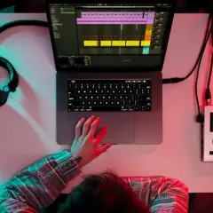 Person am Schreibtisch, um einen Beat zu machen, mit Kopfhörern, Laptop und Audio-Interface.