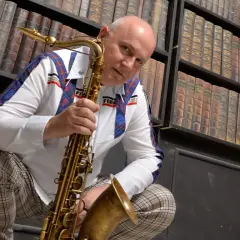 Mann mit Saxophon vor Bücherregal, bereit, einen Saxophon-VST-Sound zu erzeugen.