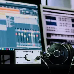 Kopfhörer und ein Verstärker liegen vor zwei Monitoren, die eine digitale Audio-Workstation zeigen. Hier wird Musik gemacht.