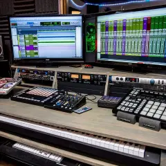 Professionelle Musikproduktion mit zwei Monitoren, die DAWs zeigen, und Geräten für die Stem-Separation.