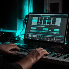 Hände spielen auf einem Keyboard, während auf dem Laptop eine Musikproduktionssoftware läuft, eine tolle fruity loops alternative.