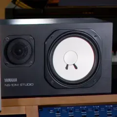 Yamaha NS-10M Studio Lautsprecher im Fokus, daneben ein Klavier und ein Bildschirm mit DAW-Software.