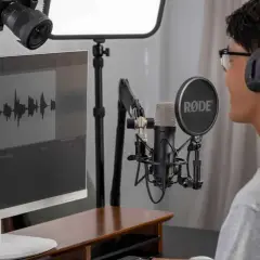 Mann mit Kopfhörern und Mikrofon, der an einem Computer sitzt und an seiner Audio-Produktion arbeitet.