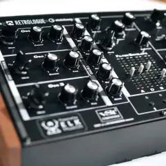 Ein schwarzes Synthesizer-Keyboard mit Holzseiten. Der "Retrologue 2" Schriftzug ist prominent platziert. Viele Regler und Schieberegler laden zum Experimentieren ein.