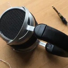 Hifiman HE400SE Test: Offene Kopfhörer mit silbernem Bügel und schwarzem Leder-Kopfband. Der 3,5mm Klinkenstecker liegt daneben.