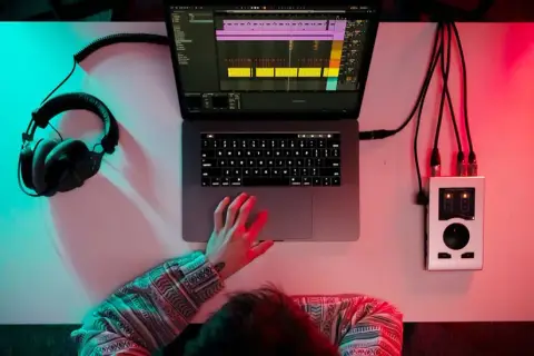Person am Schreibtisch, um einen Beat zu machen, mit Kopfhörern, Laptop und Audio-Interface.