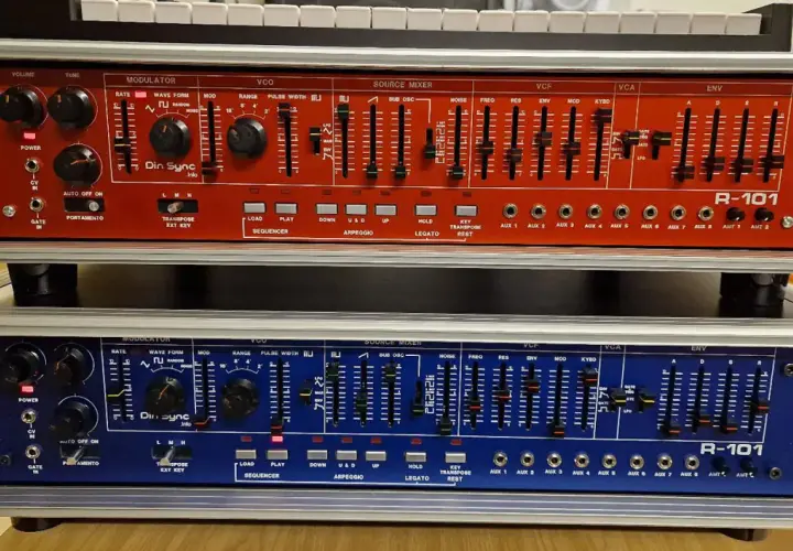 Zwei R-101 Synthesizer-Module, rot und blau, mit vielen Reglern und Schiebereglern für die Klangerzeugung. Das Din Sync Logo ist gut sichtbar.