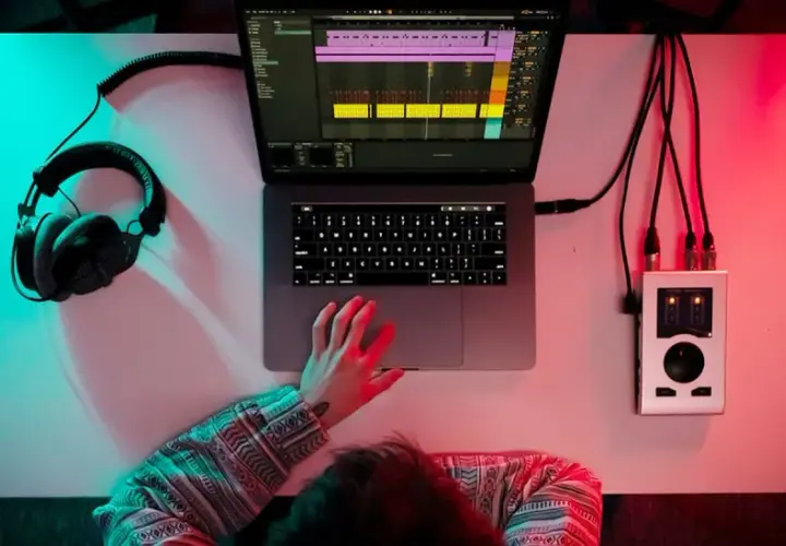 Person am Schreibtisch mit Kopfhörern, Laptop und Audio-Interface. Musikproduktion in 24 bit 48 khz.