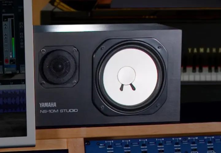 Yamaha NS-10M Studio Lautsprecher im Fokus, daneben ein Klavier und ein Bildschirm mit DAW-Software.