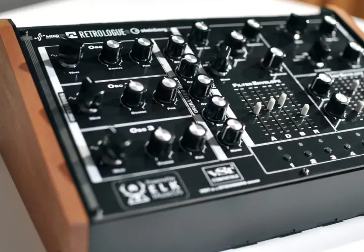 Ein schwarzes Synthesizer-Keyboard mit Holzseiten. Der "Retrologue 2" Schriftzug ist prominent platziert. Viele Regler und Schieberegler laden zum Experimentieren ein.