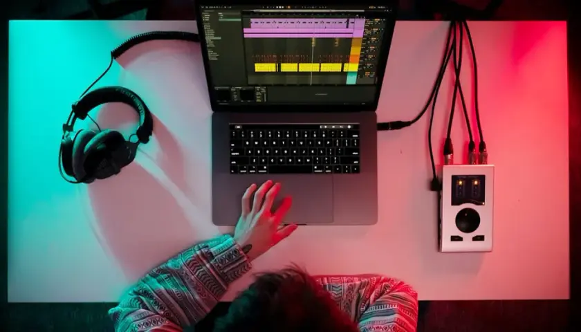 Person am Schreibtisch, um einen Beat zu machen, mit Kopfhörern, Laptop und Audio-Interface.