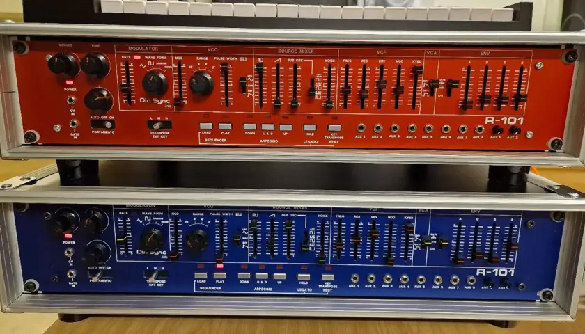 Zwei R-101 Synthesizer-Module, rot und blau, mit vielen Reglern und Schiebereglern für die Klangerzeugung. Das Din Sync Logo ist gut sichtbar.