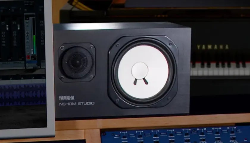 Yamaha NS-10M Studio Lautsprecher im Fokus, daneben ein Klavier und ein Bildschirm mit DAW-Software.