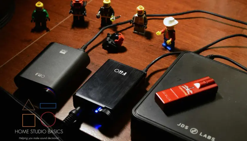 FiiO E10 und andere Audiogeräte auf einem Holztisch, umgeben von kleinen Lego-Figuren.