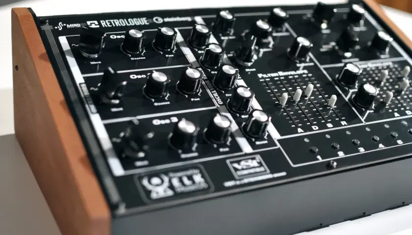 Ein schwarzes Synthesizer-Keyboard mit Holzseiten. Der "Retrologue 2" Schriftzug ist prominent platziert. Viele Regler und Schieberegler laden zum Experimentieren ein.