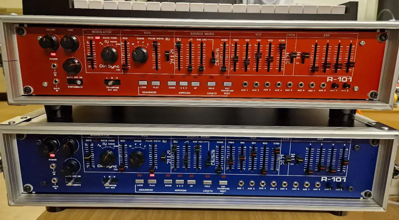 Zwei R-101 Synthesizer-Module, rot und blau, mit vielen Reglern und Schiebereglern für die Klangerzeugung. Das Din Sync Logo ist gut sichtbar.