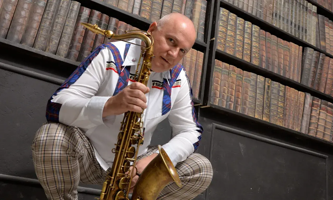Mann mit Saxophon vor Bücherregal, bereit, einen Saxophon-VST-Sound zu erzeugen.
