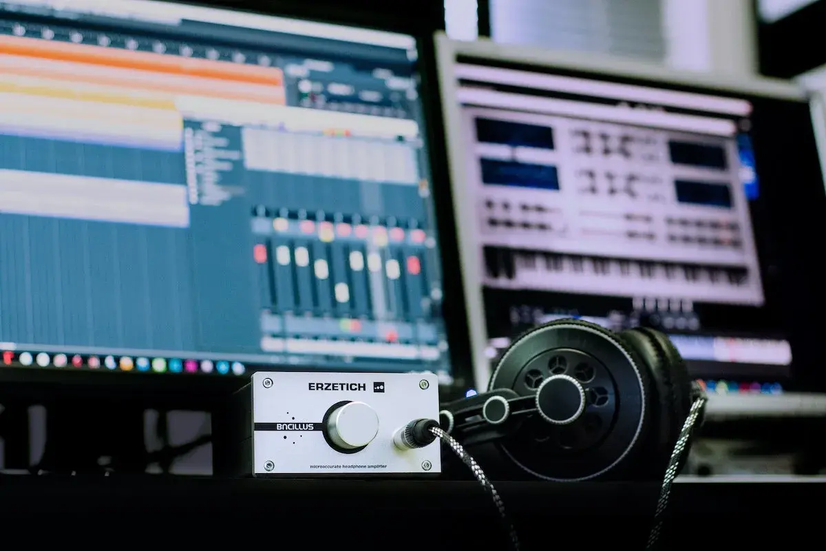 Kopfhörer und ein Verstärker liegen vor zwei Monitoren, die eine digitale Audio-Workstation zeigen. Hier wird Musik gemacht.