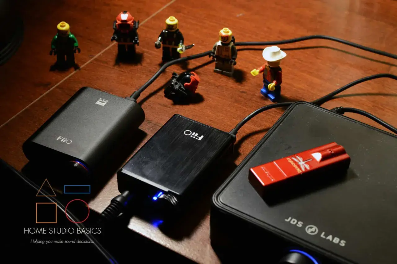 FiiO E10 und andere Audiogeräte auf einem Holztisch, umgeben von kleinen Lego-Figuren.