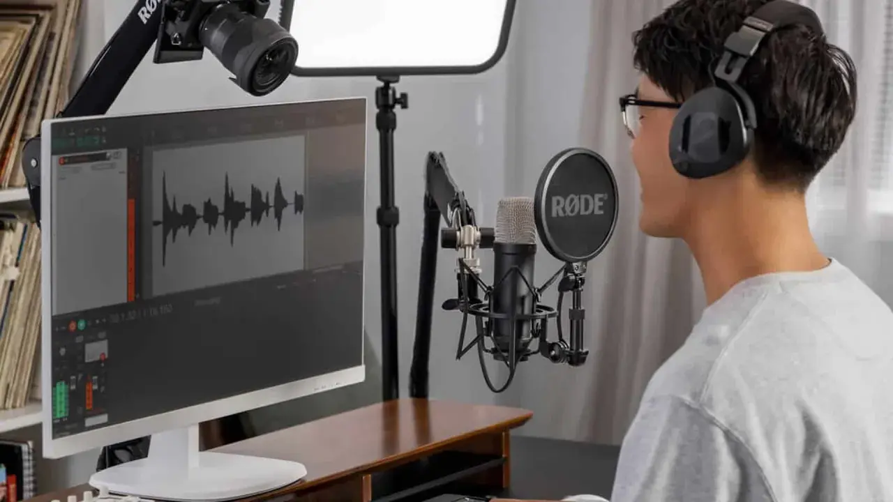 Mann mit Kopfhörern und Mikrofon, der an einem Computer sitzt und an seiner Audio-Produktion arbeitet.