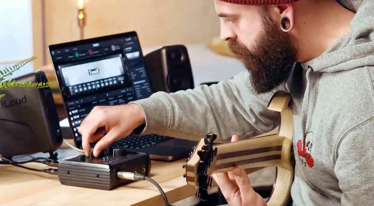 Mann mit Bart spielt Gitarre und bedient ein Audio-Interface, während er auf einem Laptop mit der **ToneX**-Software arbeitet.