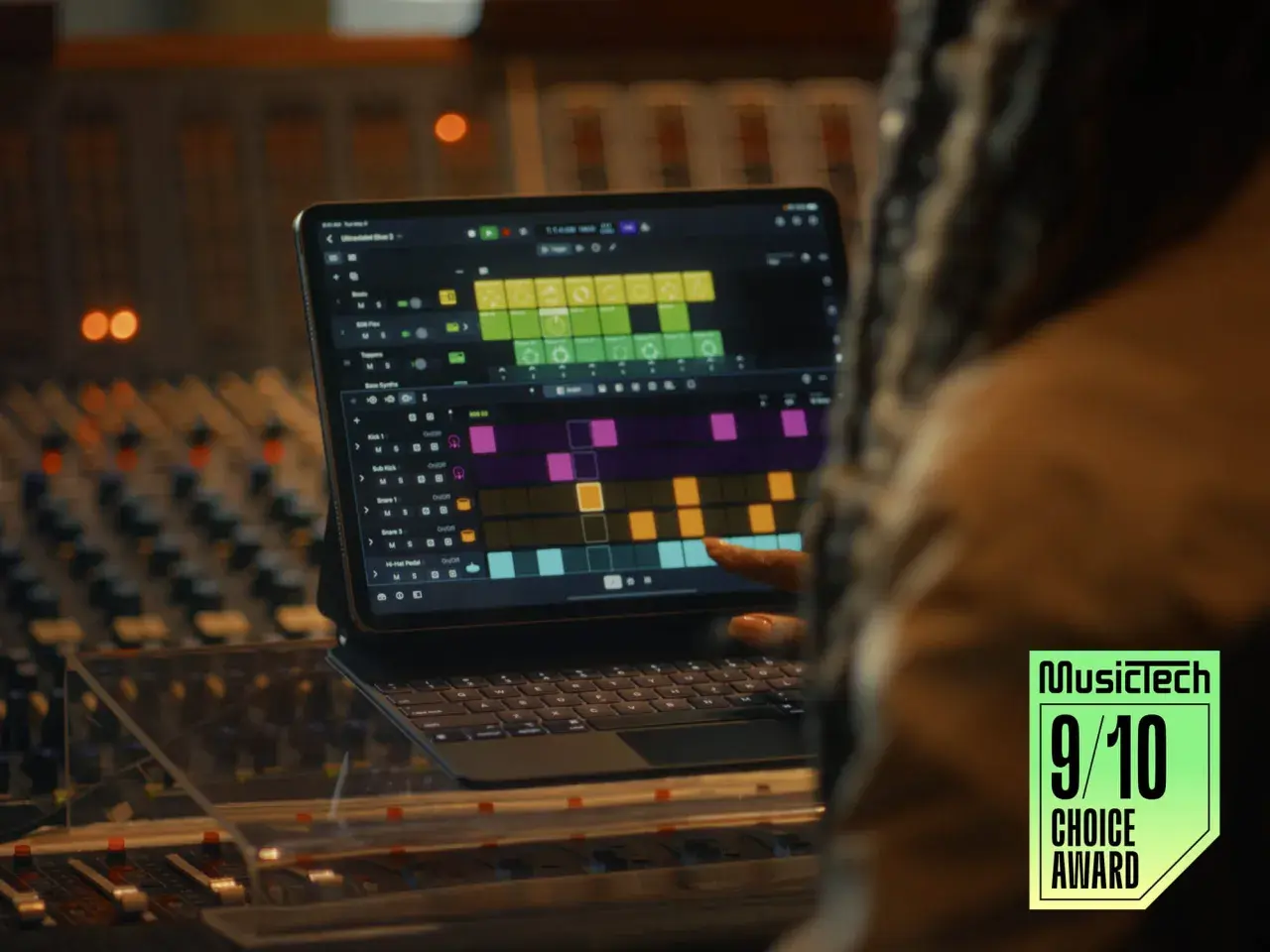 Ein Finger tippt auf einem iPad mit Logic Pro auf eine Drum-Spur. Ein Musikproduzent arbeitet im Studio.