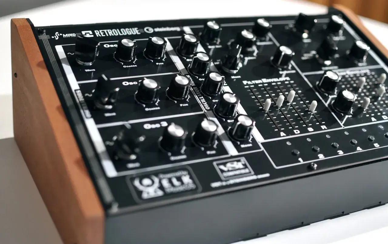 Ein schwarzes Synthesizer-Keyboard mit Holzseiten. Der "Retrologue 2" Schriftzug ist prominent platziert. Viele Regler und Schieberegler laden zum Experimentieren ein.