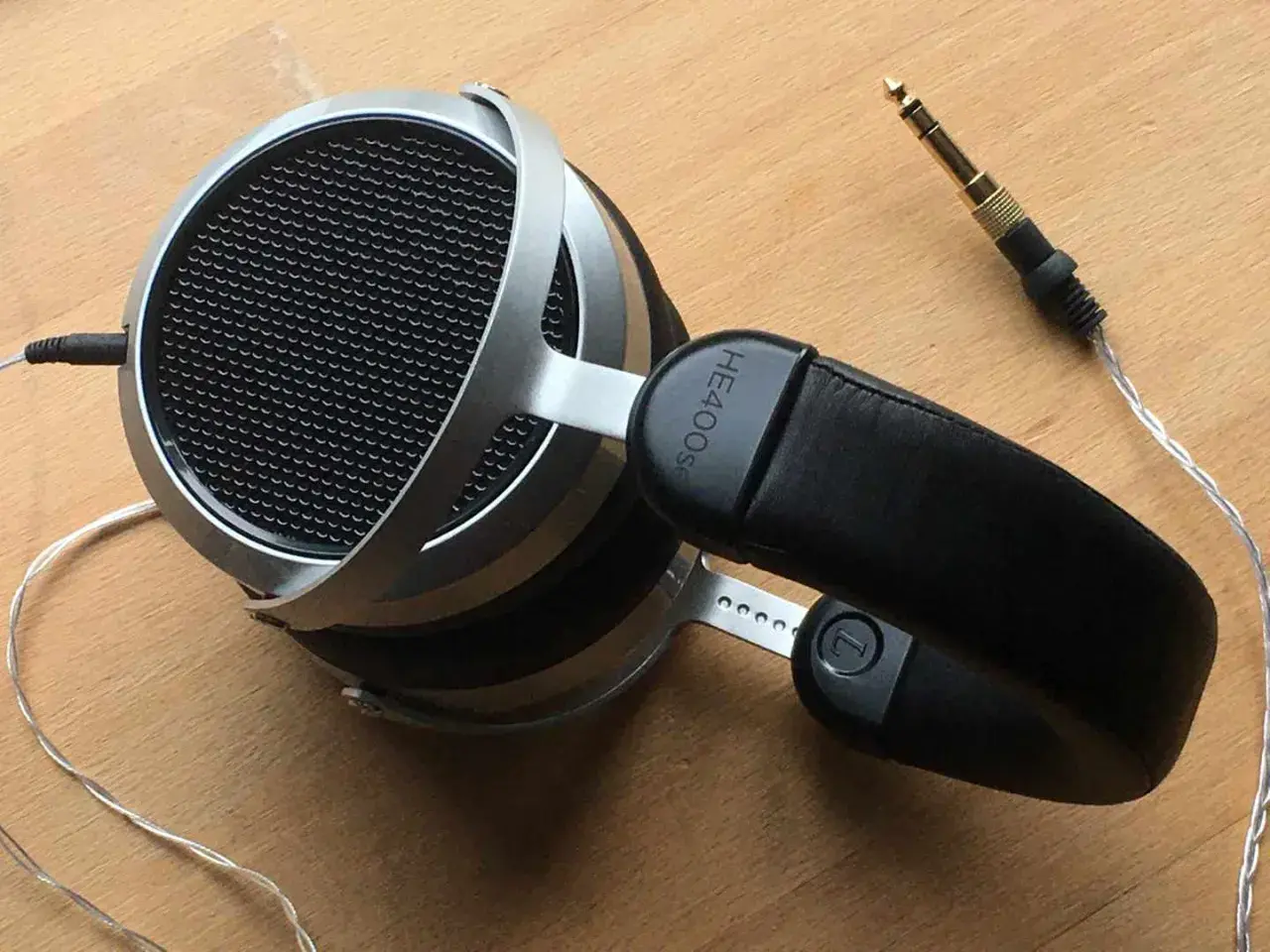 Hifiman HE400SE Test: Offene Kopfhörer mit silbernem Bügel und schwarzem Leder-Kopfband. Der 3,5mm Klinkenstecker liegt daneben.
